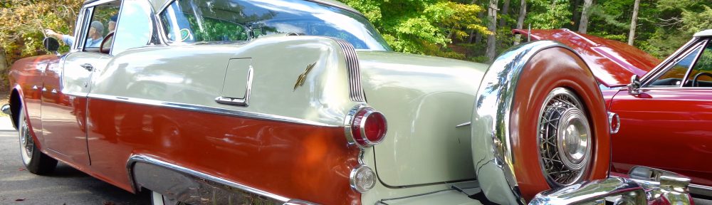 Classic two-tone vintage car parked on grass with trees in the background.